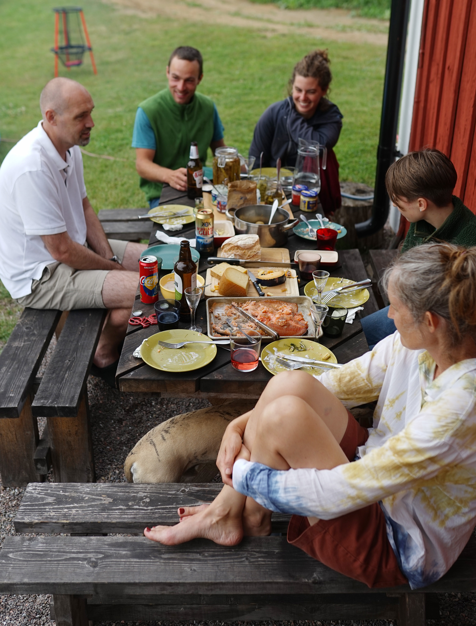 Eine Gruppe von Menschen unterhält sich draußen, während sie um einen Tisch herum essen.